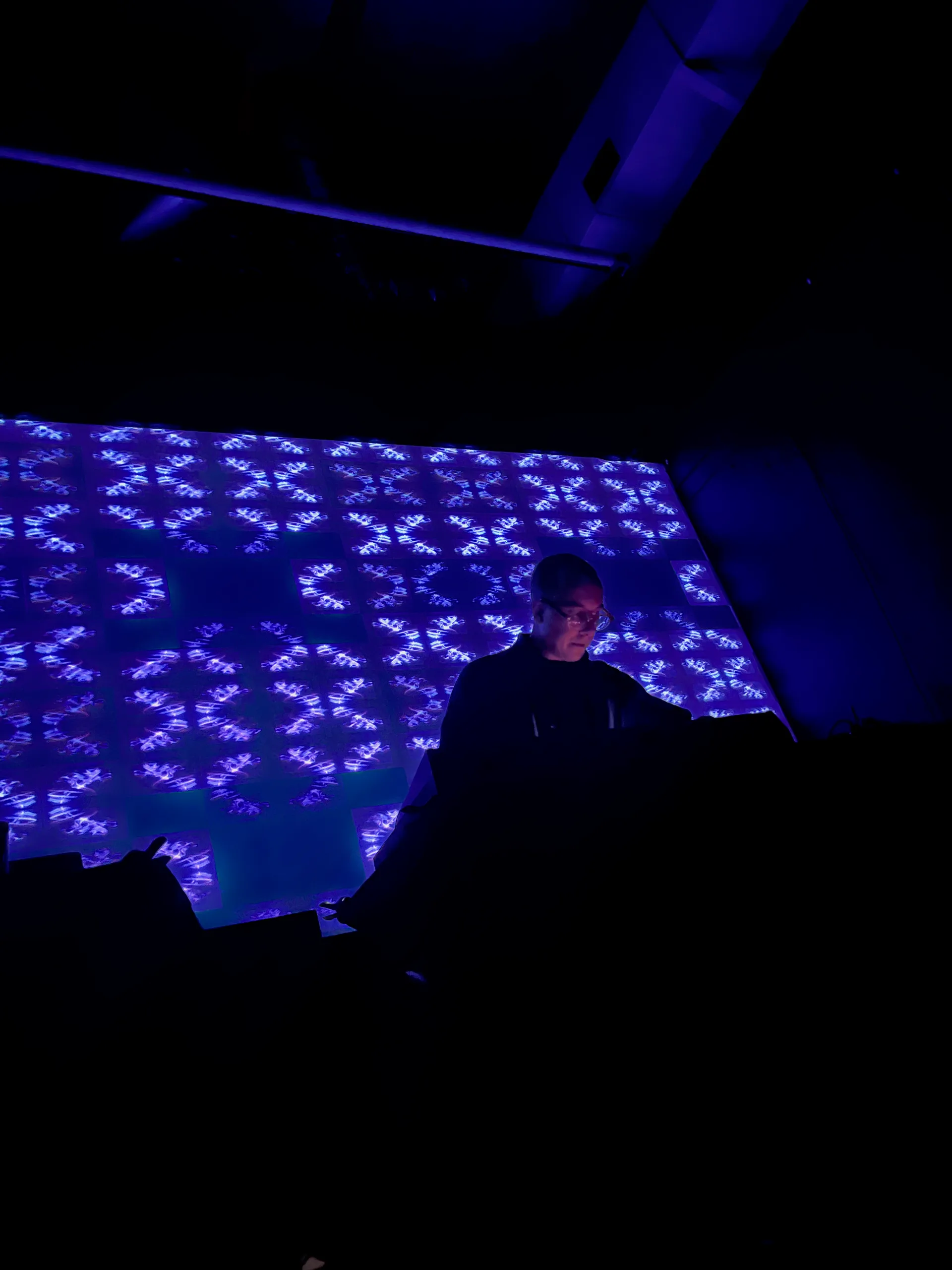 Triangular Waves performing music in front of an abstract pattern with blue color.